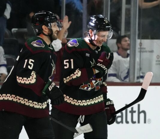 Arizona Coyotes defenseman Troy Stecher (51) and Coyotes center Alexander Kerfoot (15) celebrate a goal by Coyotes' Michael Carcone against the Tampa Bay Lightning during the first period of an NHL hockey game Tuesday, Nov. 28, 2023, in Tempe, Ariz. (AP Photo/Ross D. Franklin)