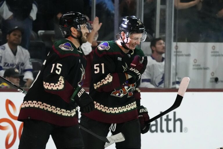 Arizona Coyotes defenseman Troy Stecher (51) and Coyotes center Alexander Kerfoot (15) celebrate a goal by Coyotes' Michael Carcone against the Tampa Bay Lightning during the first period of an NHL hockey game Tuesday, Nov. 28, 2023, in Tempe, Ariz. (AP Photo/Ross D. Franklin)