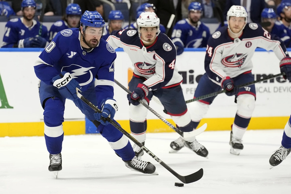 Tampa Bay Lightning left wing Nick Paul (20) works around Columbus Blue Jackets center Cole Sillinger (4) and right wing Mathieu Olivier (24) on his way to scoring a goal during the second period of an NHL hockey game Tuesday, Dec. 17, 2024, in Tampa, Fla. (AP Photo/Chris O'Meara)