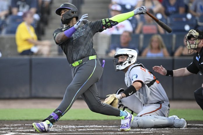 Tampa Bay Rays' Junior Caminero, left, watches the flight of the ball after hitting a three-run home run as Baltimore Orioles catcher Jacob Stallings and home plate umpire Sean Barber, right, look on during the first inning of a baseball game, Friday, July 18, 2025, in Tampa, Fla. (AP Photo/Phelan M. Ebenhack)